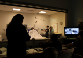 Simulation faculty use a two-way mirror to observe nursing students in the Escape Room.