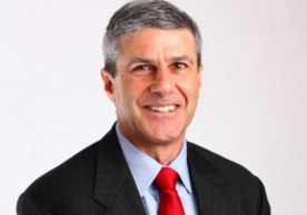 A headshot of David King in a dark suit with a red tie.